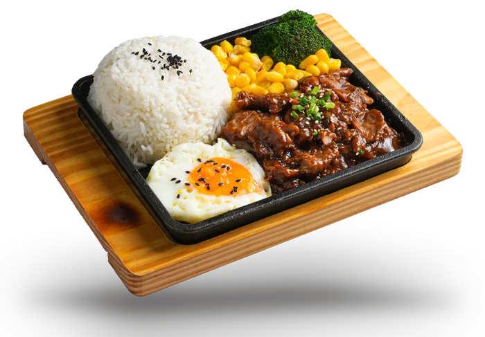 Sizzling beef and rice on a cast-iron plate with a fried egg, sweetcorn and broccoli