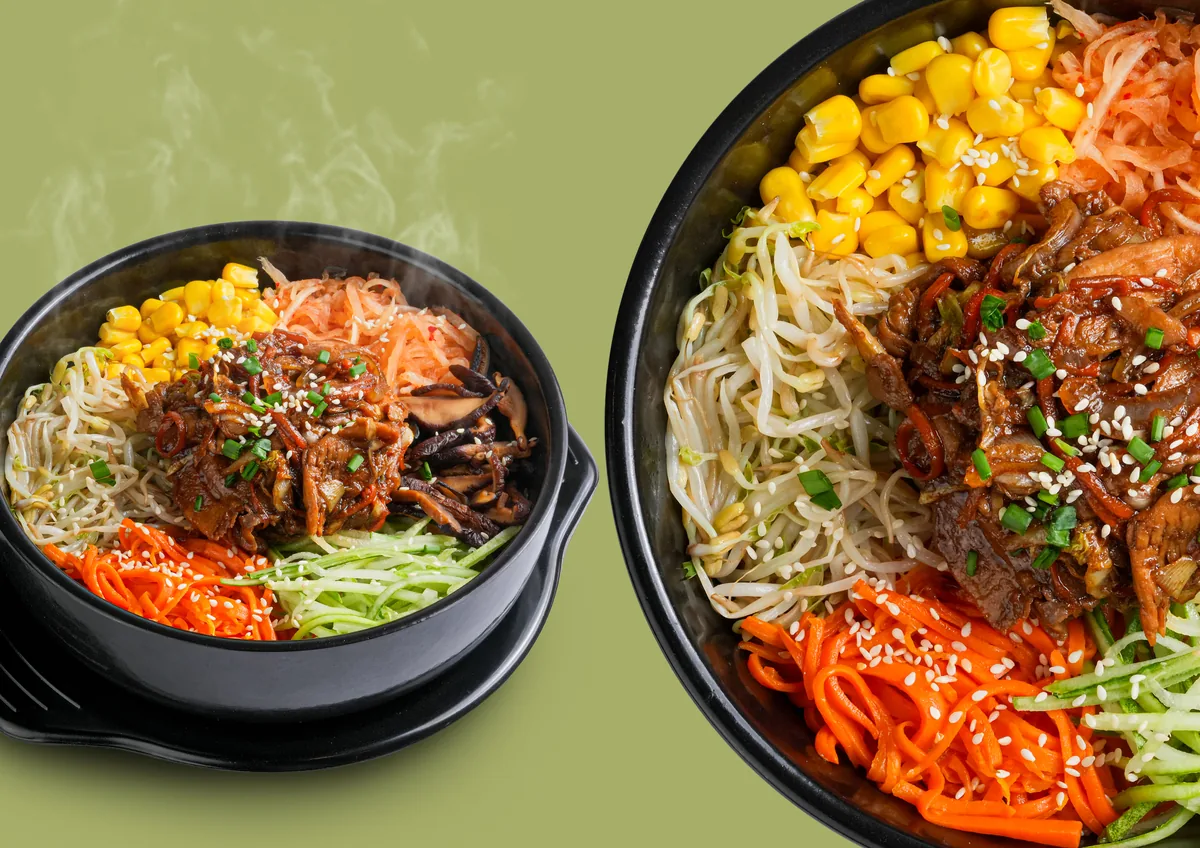 Food photography of two black bowls of bulgogi bibimbap with corn, beansprouts, carrot and cucumber