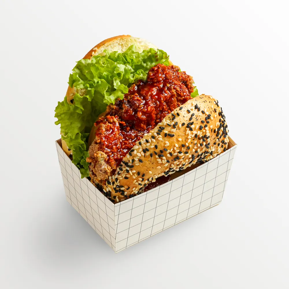 Fried chicken burger with lettuce and chilli sauce in a printed takeaway box