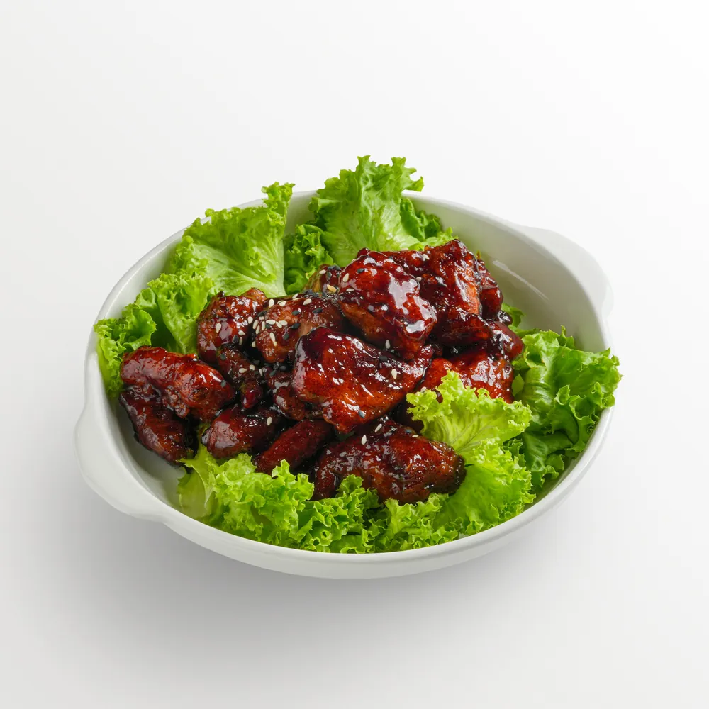 White background food photography of glazed soy-garlic chicken with sesame seeds on lettuce