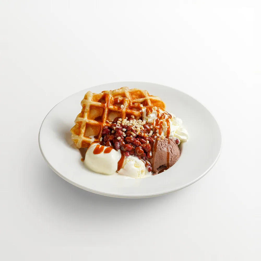 Waffle with vanilla and chocolate ice cream, red bean, crushed peanuts, whipped cream and caramel sauce on a white plate