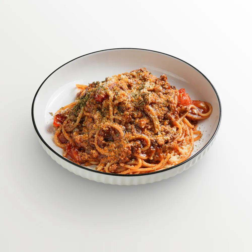 Spaghetti bolognese topped with parmesan and herbs in a fluted bowl