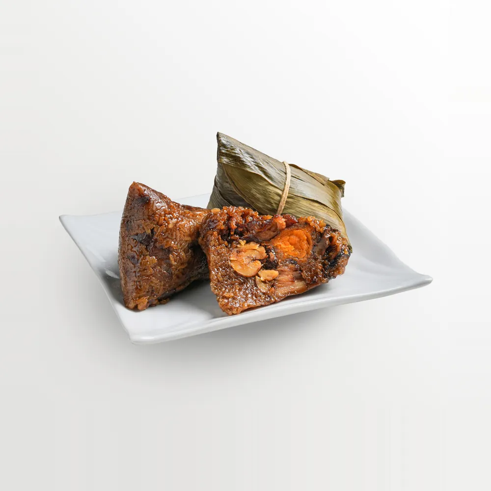 Two bak chang — glutinous rice dumplings in bamboo leaf, one cut open