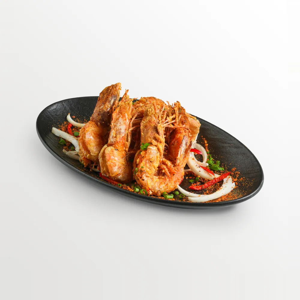 White background food photography of salted-egg fried prawns with chilli, onion and spring onion on a black oval plate